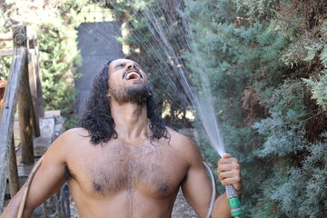 Seductive long haired man getting wet with hose