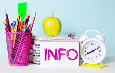 On a light table there are books, stationery, a white alarm clock, an apple. Next to it is a...