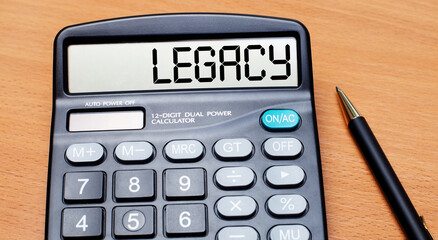 On a wooden table there is a black pen and a calculator with the text LEGACY. Business concept