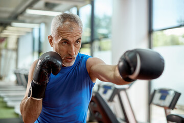 Mature man exercises boxing during sports training at gym.
