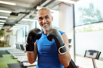 Fototapeta na wymiar Happy mature man exercises boxing while working out at gym and looking at camera..