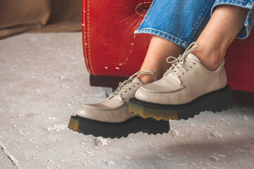 Female legs with leather shoes. Teenage sneakers close-up. Teen girl sitting on old leather chair...