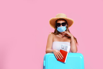 Young woman waiting for flight, sitting on floor near her suitcase, wearing face mask to prevent coronavirus