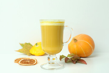Glass of pumpkin latte and ingredients on white background