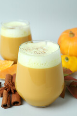 Glasses of pumpkin latte and ingredients on light gray background