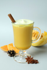 Glass of pumpkin latte and ingredients on light gray background