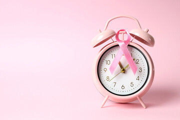 Breast cancer awareness ribbon and alarm clock on pink background