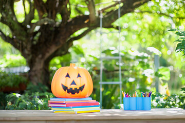 Pumpkin and colorful books in outdoor under tree.Fall homeschooling, schooling concepts.Halloween in school.Jack-o-lantern and education.Fun autumn lesson.