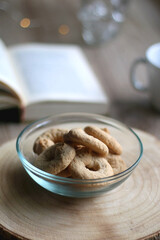 Bowl of cookies, cup of hot beverage, open book and lit candles on a table. Selective focus.