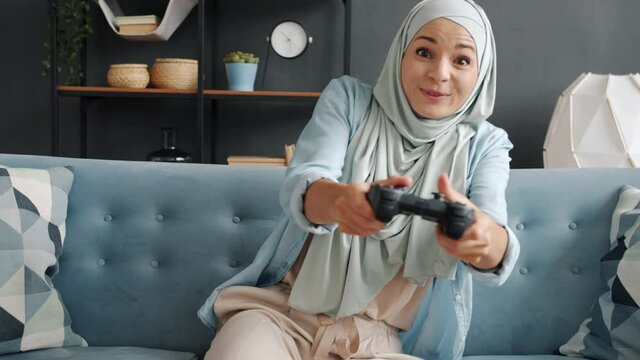 Slow motion portrait of happy muslim girl skillful gamer playing alone enjoying videogame laughing at home. Islam and entertainment concept.
