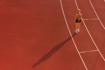 young woman in sportswear stands on the stadium treadmill, back view. concept of sports training, fitness, healthy lifestyle.