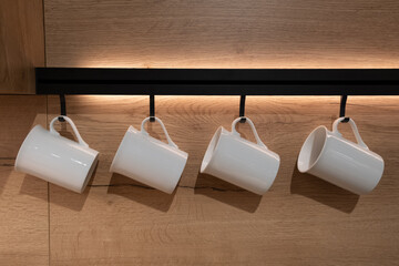 Set of empty drinking white ceramic cups mugs hanging  on a stand in the kitchen decoration on a...