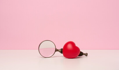 red heart and magnifier on white table, pink background