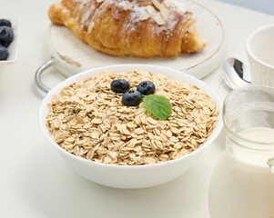 Raw oatmeal in white ceramic plate on white table, breakfast