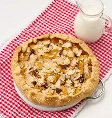 baked round pie with apple pieces, sprinkled with almond flakes on a white table