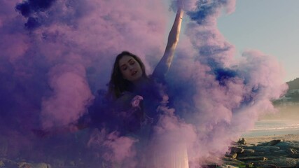 woman dancing with purple smoke bomb on beach celebrating creative expression with playful dance spin in slow motion