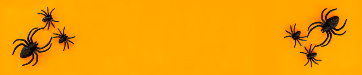 Flat lay banner of black horror spiders of different sizes directed in different directions on orange backdrop with copy space. Halloween decoration spooky background concept for holidays