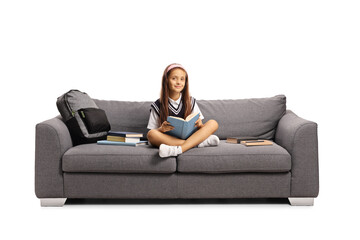 Fototapeta na wymiar Schoolgirl in a uniform sitting on a couch and reading a book