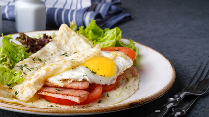Omelet with fried egg, bacon and tomatoes on a plate.