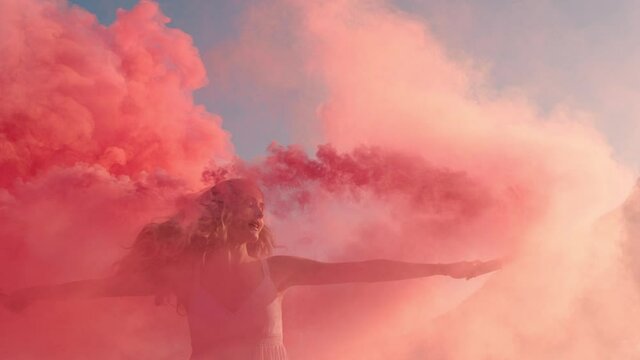 woman dancing with pink smoke bomb on beach at sunrise celebrating creative freedom with playful dance spin slow motion