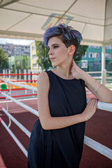 Stylish millennial girl with purple colored hair wearing little black dress at the school stadium during graduation party, generation Z, fashion and diversity, girl power, outdoor lifestyle