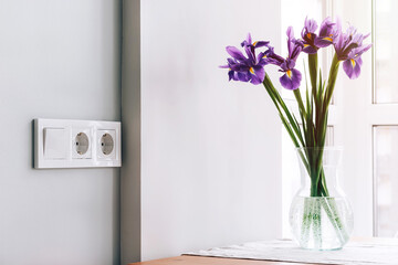 White european electrical outlets and switch on gray wall in light modern kitchen with bouquet of...