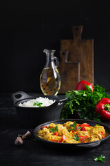 Traditional Indian curry chicken masala. Indian chicken curry with sweet peppers and  rice in bowl, spices, dark background. Traditional Indian dish.