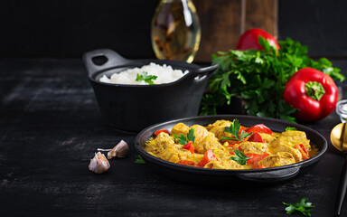 Traditional Indian curry chicken masala. Indian chicken curry with sweet peppers and  rice in bowl, spices, dark background. Traditional Indian dish.