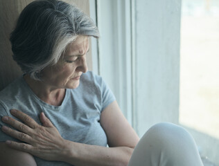 Obraz premium Elderly senior sick disabled, sad woman in pain and suffering sitting by the window in the hospital. Untreatable illness and loss of loved ones, suffering and loneliness