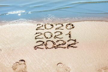 Fototapeta premium The numbers 2021, 2022 are drawn on the sand and washed away by the wave, the symbol of the new year, the change of the year
