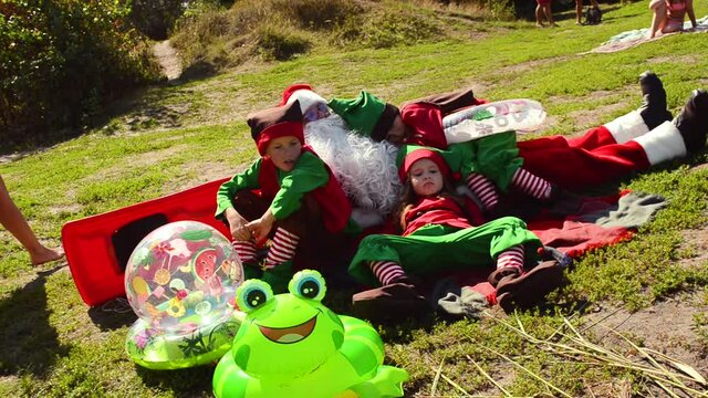 Elves and Santa Claus sunbathe on the beach by the water in summer in a winter coat and costumes. The concept of rest in warm countries