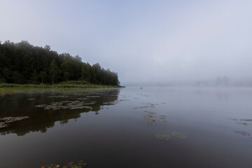Mystical landscape at dawn. Early morning. Fog on the river. Beautiful dawn in the summer by the river. A man floats in a boat against the background of dawn.
