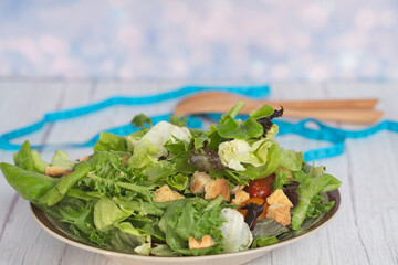 A serving of garden salad, wooden fork and spoon with measuring tape. Selective focus points. Blurred background