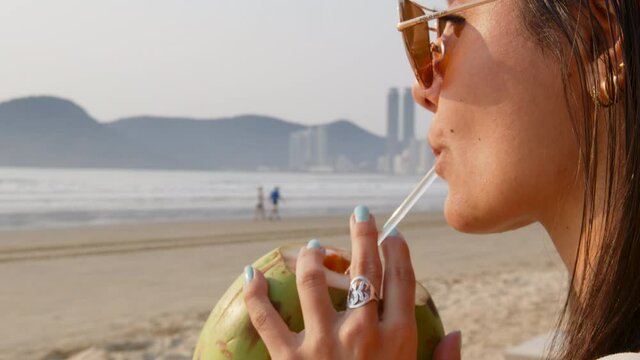 Woman drinking coconut water early morning at Balne&aacute;rio Cambori&uacute;, Brazil.