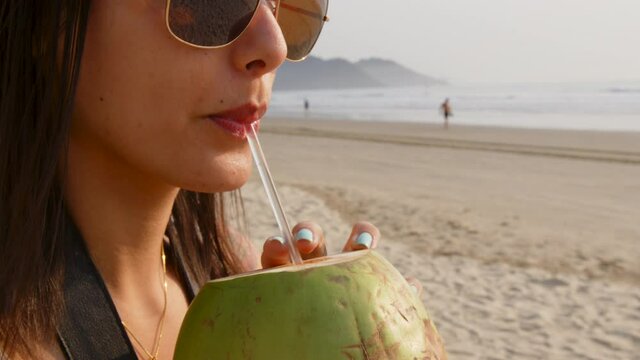Woman drinking coconut water at the Balne&aacute;rio Cambori&uacute; beach, Brazil.