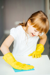 portrait of a girl cleans up a white table in yellow gloves with a blue sponge