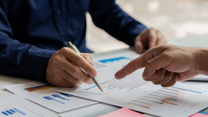 Two young businessmen with pens pointing to graph papers in a meeting of financial managers discussing the success of the company's growth programme. financial statistics in the office at the laptop a