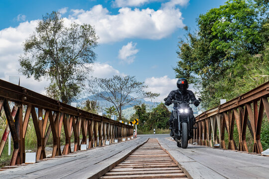 man riding his motorcycle over temporary bridge in north Thailand