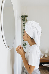 Filipino woman looking into a mirror while drying her hair and using an eye mask