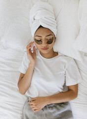 Young Filipino woman laying on bed while drying hair and wearing an eye mask
