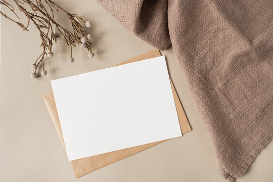 Blank paper sheet card with mockup copy space and dry floral branch and blanket cloth on neutral beige background. Minimal aesthetic wedding invitation template. Flat lay, top view