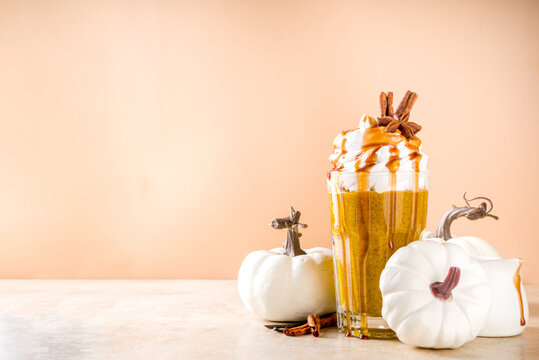 Pumpkin spice latte or milkshake,traditional autumn hot drink with anise, cinnamon, caramel topping, on warm colored background with small decorative pumpkins and cozy sweater, 