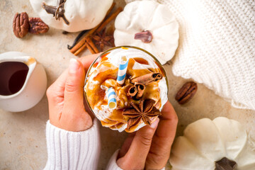 Pumpkin spice latte or milkshake,traditional autumn hot drink with anise, cinnamon, caramel topping, on warm colored background with small decorative pumpkins and cozy sweater,
