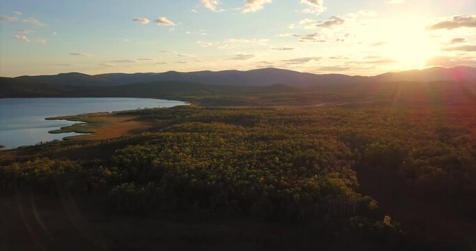 Aerial view of an amazing lake Blagodatnoe with blue water and wide green forests growing on its banks. Hills are on the background. Evening. The Far East of Russia