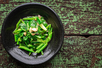 stir fried collards with salted fish and garlic in black ceramic plate on green old wood texture background with copy space for text, top view, collard greens