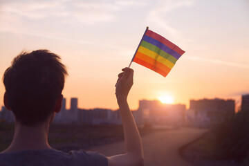 Transgender woman holding rainbow flag on sky city background, LGBTQ pride, parade, march concept