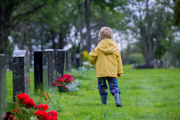 Sad little child, blond boy, standing in the rain on cemetery, sad person, mourning