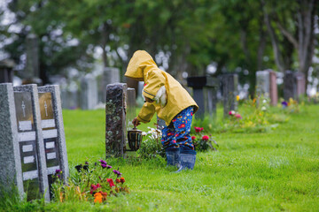 Sad little child, blond boy, standing in the rain on cemetery, sad person, mourning