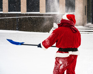 Winter time. Santa Claus with a shovel removes snow on a snowy street. View from back.
