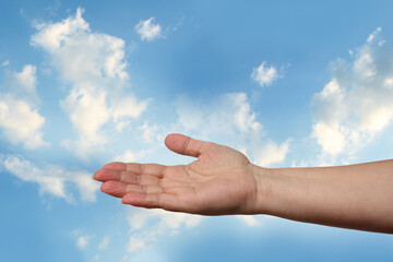 female hand outstretched against beautiful summer landscape, blue sky with clouds, concept of transcendence, infinity, height, the kingdom of God